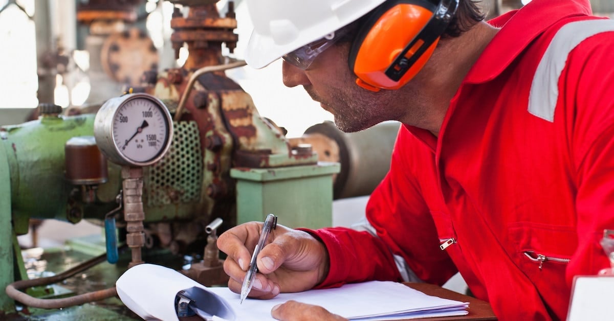 Worker noting gauge at oil refinery