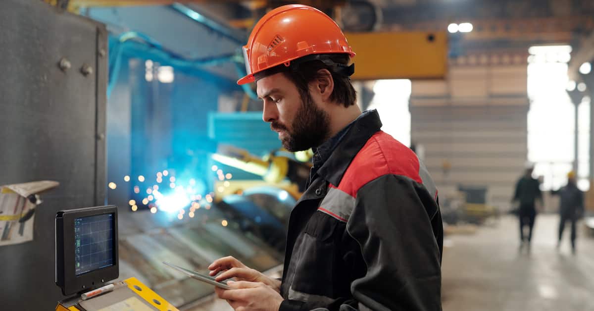 Side view of young engineer in workwear using digital tablet
