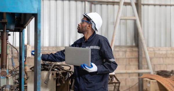 Male engineer in uniform using laptop for machinery inspection
