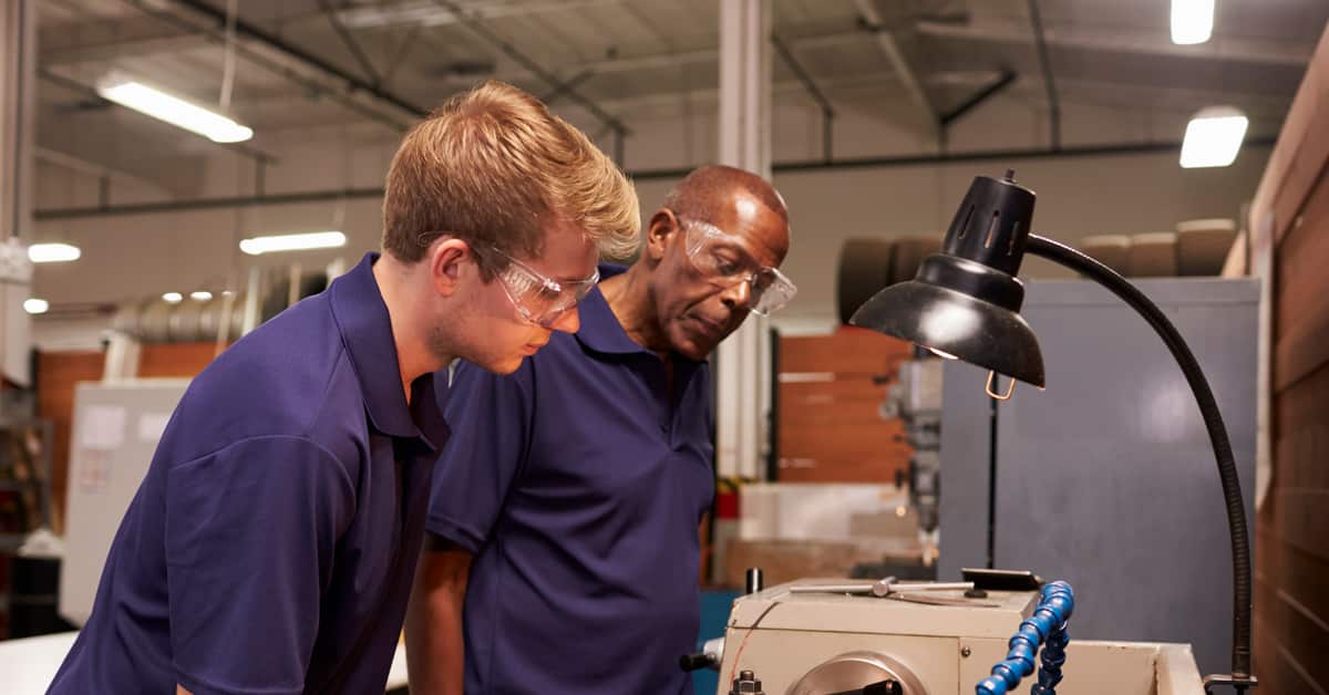 Engineer training male apprentice on milling machine