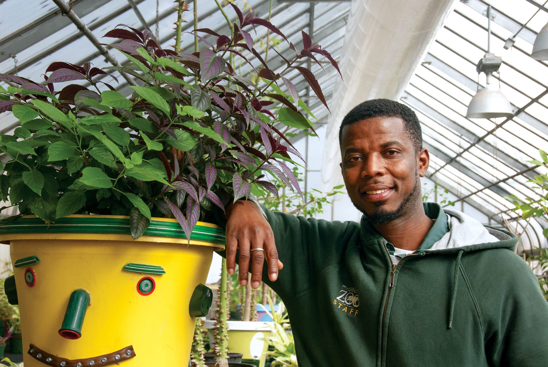 A Philadelphia Zoo employee smiles next to a decorated planter in the Zoo's greenhouse.