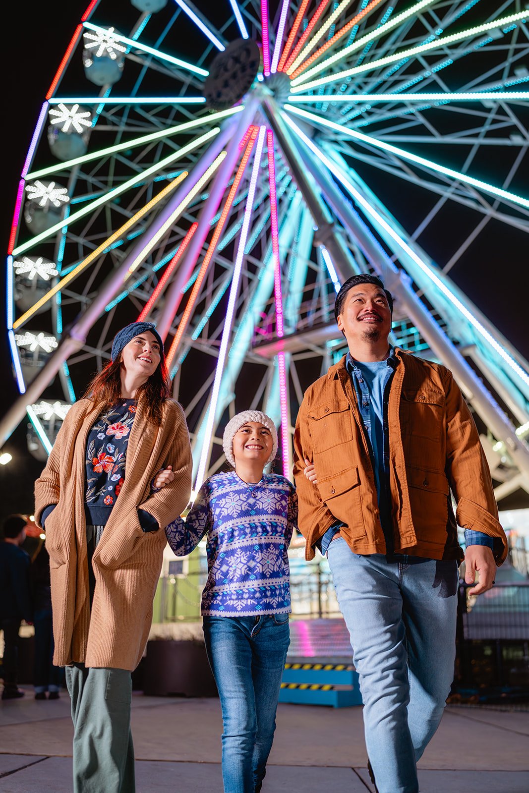 A family of three smiles for a photo with the Philly Zoo ferris wheel in the background.