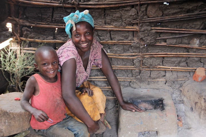 A woman and her child pose smiling next to a mud stove.