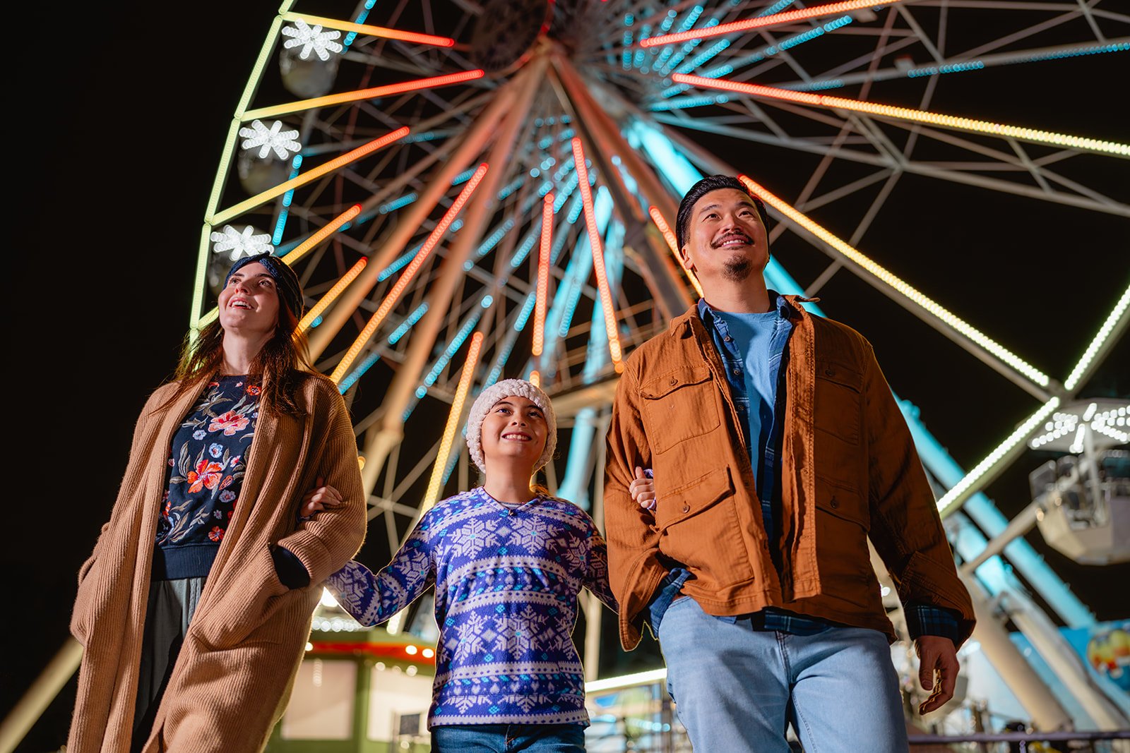 A family of three smiles for a photo with the Philly Zoo ferris wheel in the background.