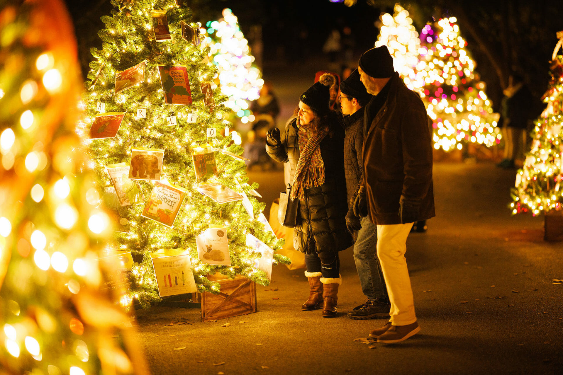 A family stands in front of a decorated tree in the Our Neck of the Woods display at Philadelphia Zoo's LumiNature.