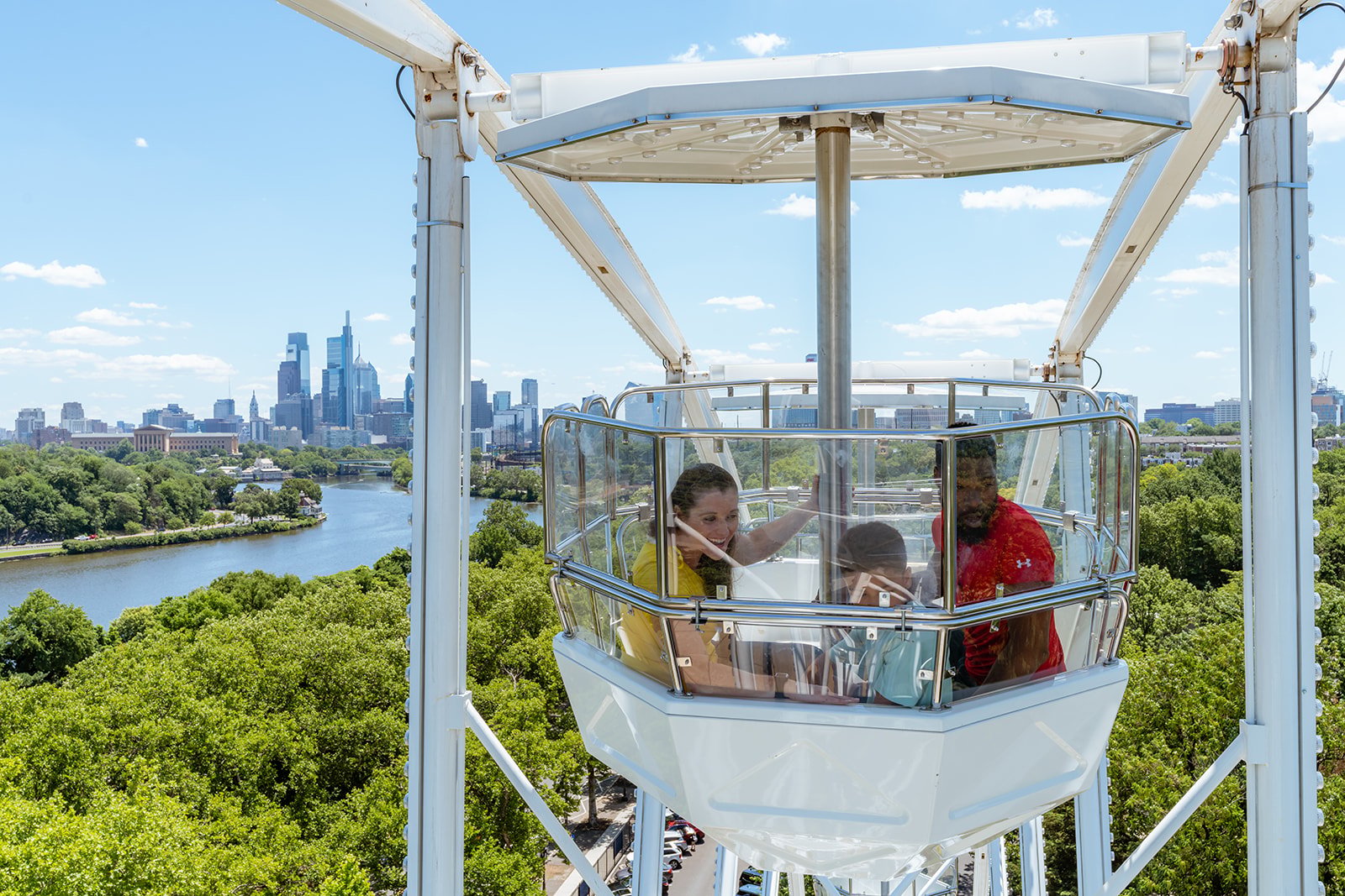 A family rides the Philly Zoo Pherris Wheel, looking out at the view of the Zoo and the city of Philadelphia in the distance.