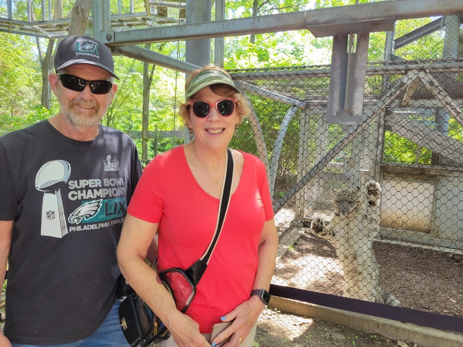 A man and a woman stand in front of a snow leopard smiling