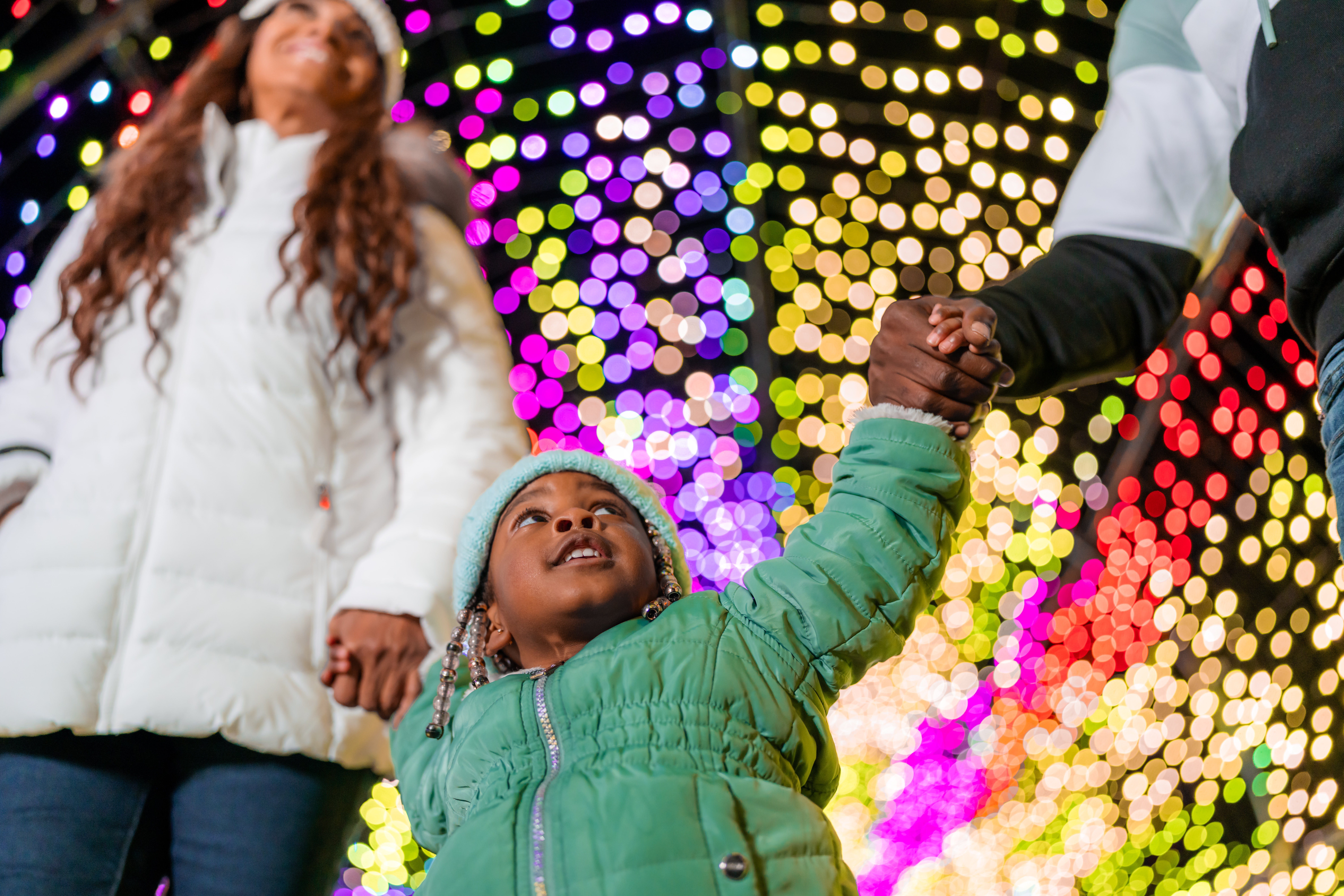 A child holds her parents' hands and looks with wonder at the lights in the tunnel at LumiNature, Philadelphia Zoo's holiday light show.