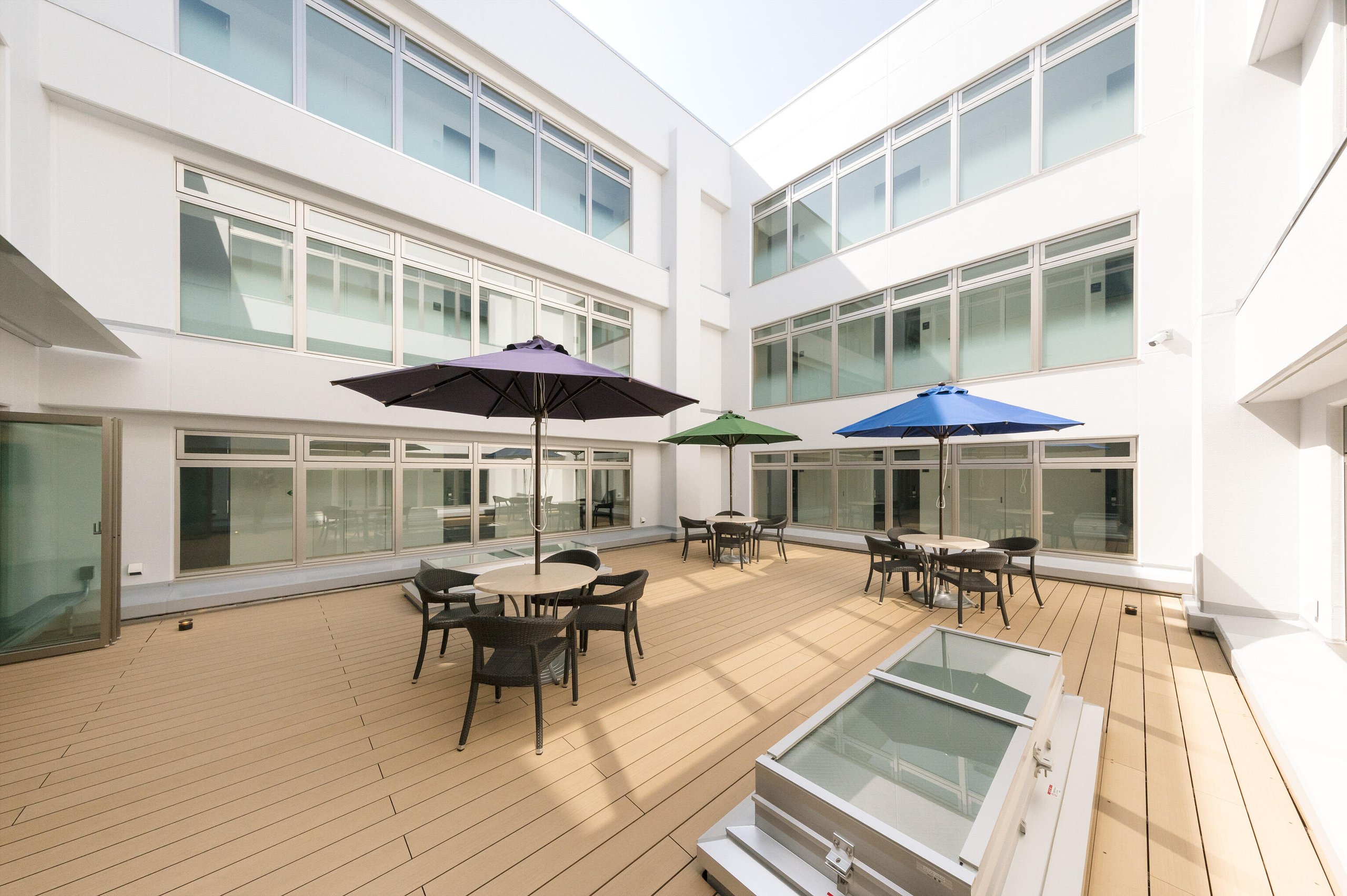 A spacious outdoor terrace with wooden decking and tables shaded by colorful umbrellas.