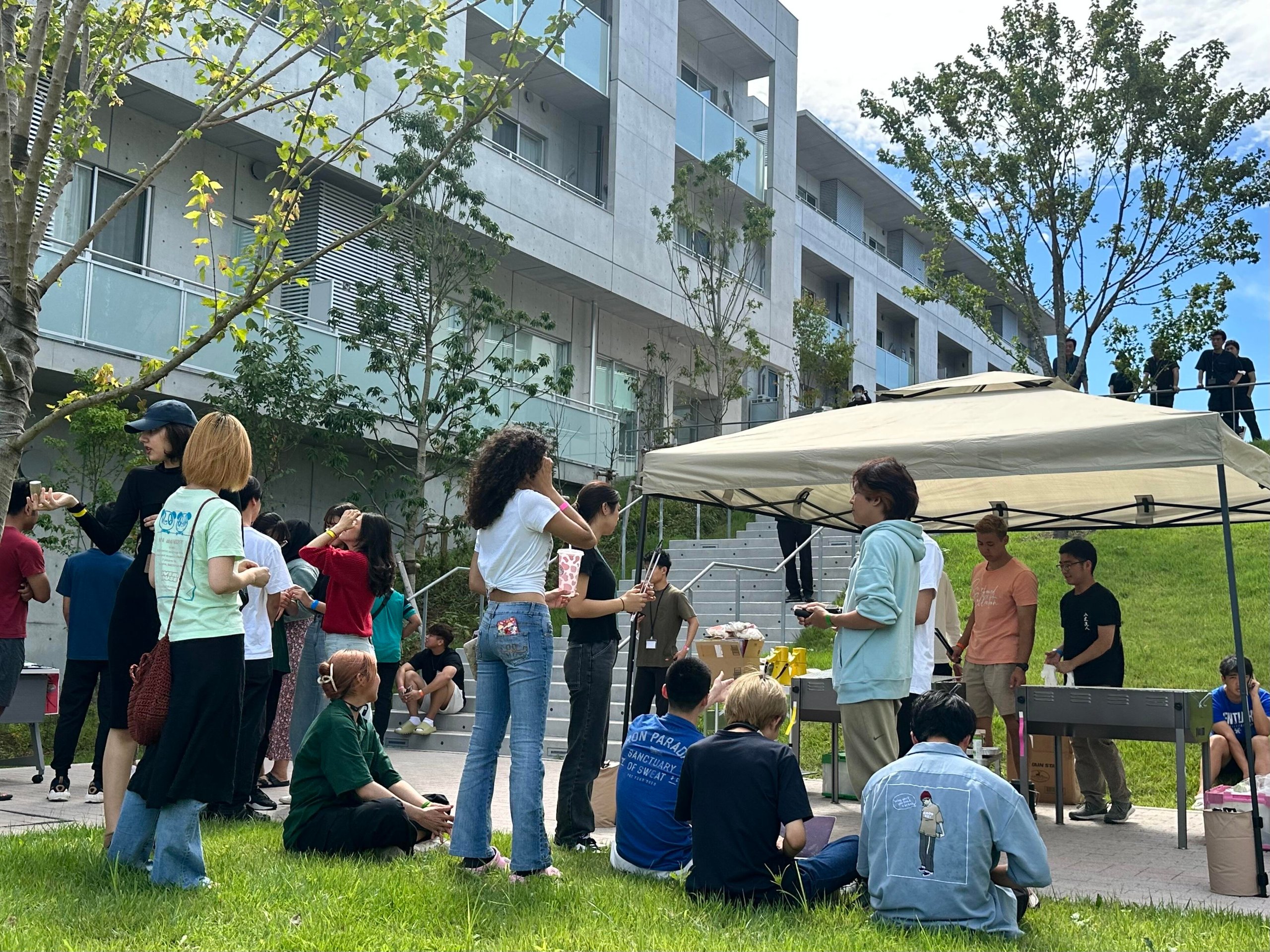 A group of young people enjoying a barbecue in the courtyard of a modern concrete building.