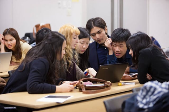 Students working together around a laptop during a group discussion in a classroom.