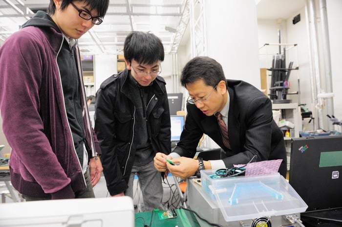 教師が2名の学生に何かを教えている写真。