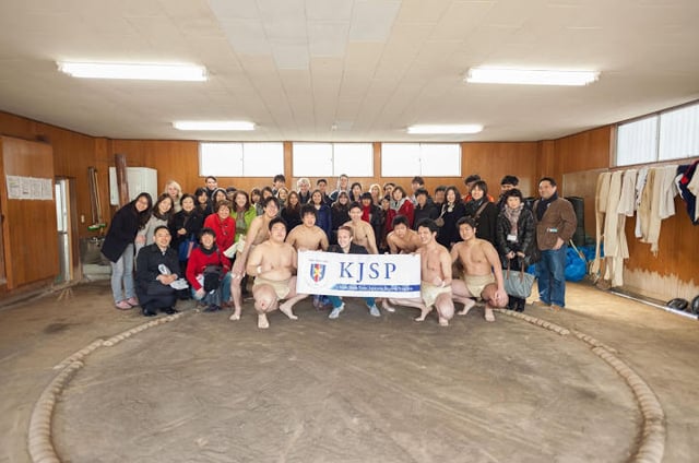 Participants of the KJSP program posing with sumo wrestlers in a sumo training ring.