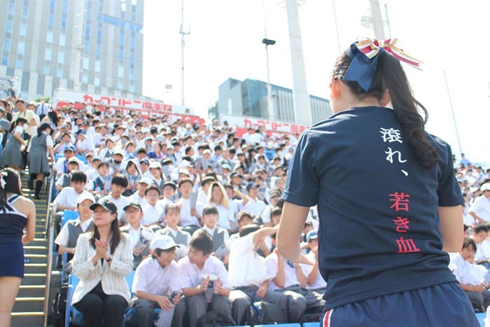 「陸の王者、若き血」と背中に書かれたTシャツを着て応援するチアリーダーと学生。