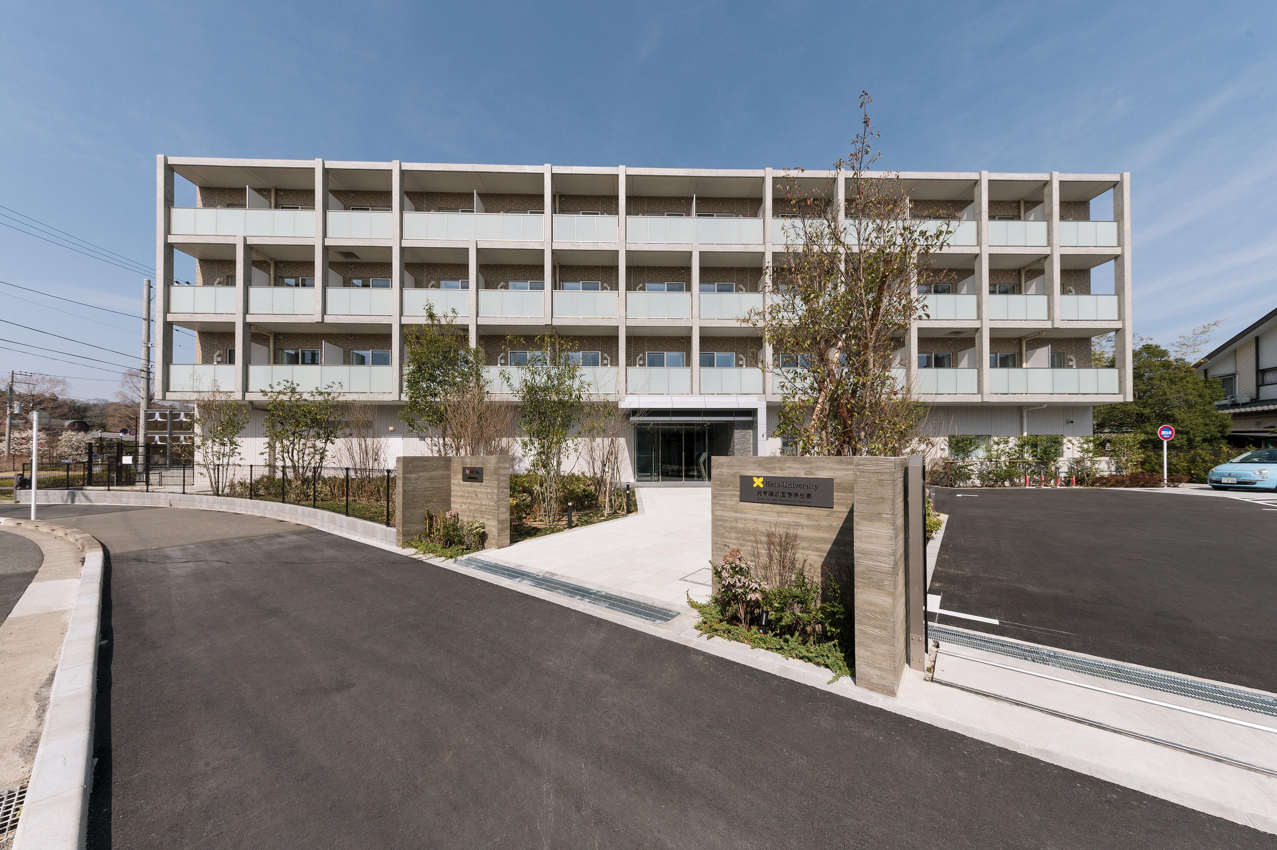 The exterior and main entrance of a modern multi-story residential building under a clear blue sky.