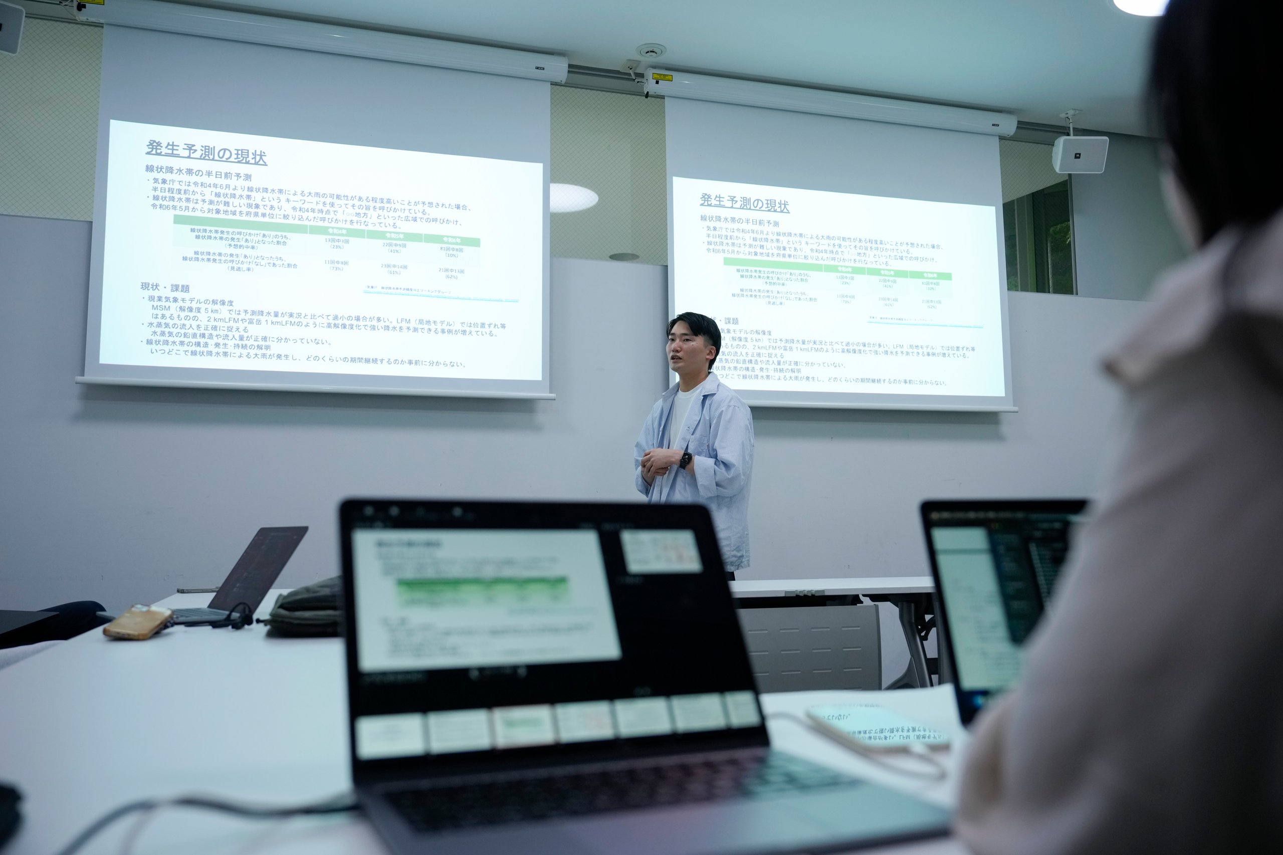 A laptop in the foreground and a student giving a presentation in the background
