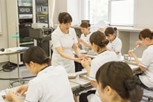 看護演習で、教員から手元の細かい動作について直接指導を受ける学生たち。