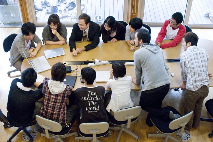 教室で複数の人物がディスカッションしている写真。