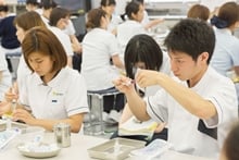 看護実習室で、真剣な表情で注射器の操作を練習する白衣姿の学生たち。