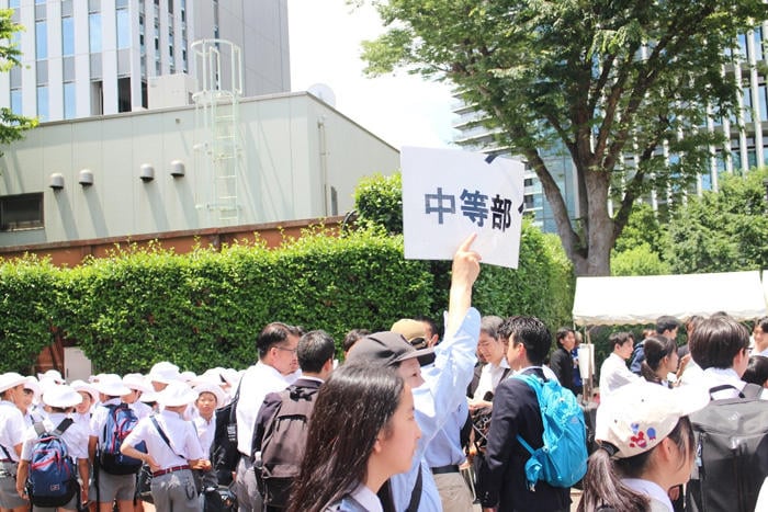 「中等部」のプラカードを掲げる人と集合する学生たち。