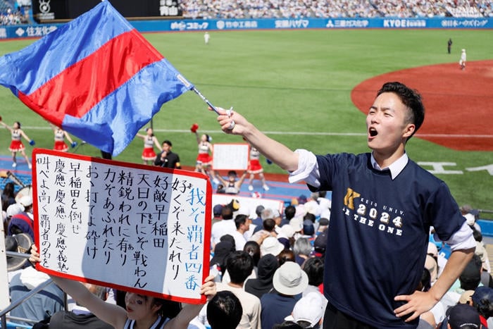 応援歌の歌詞ボードを掲げ、三色旗を振って応援する学生。