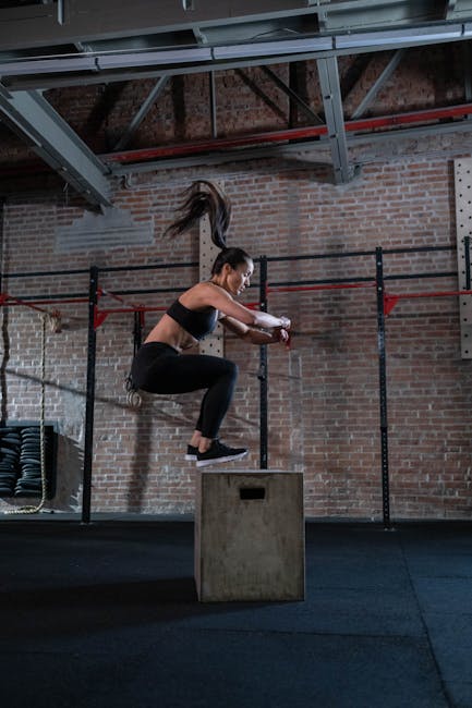 A fit woman executes a box jump in a gym setting, showcasing athleticism and fitness.