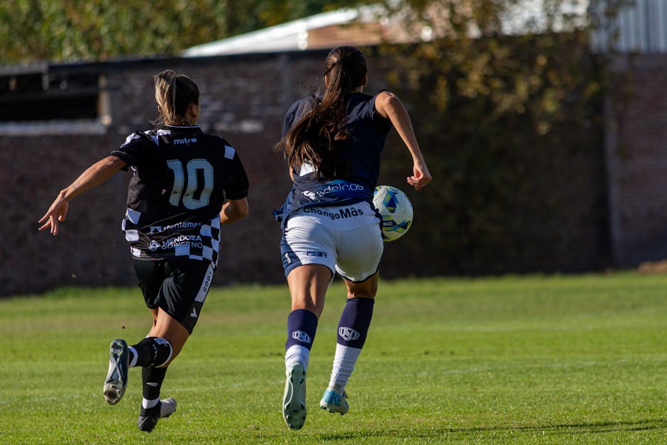Exciting capture of two female soccer players in action on the field during a sunny day.