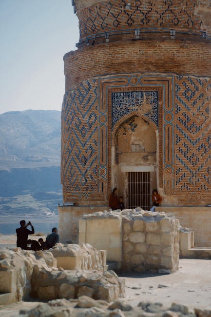 Historic ornate structure in a desert setting with distant mountains and visitors exploring.