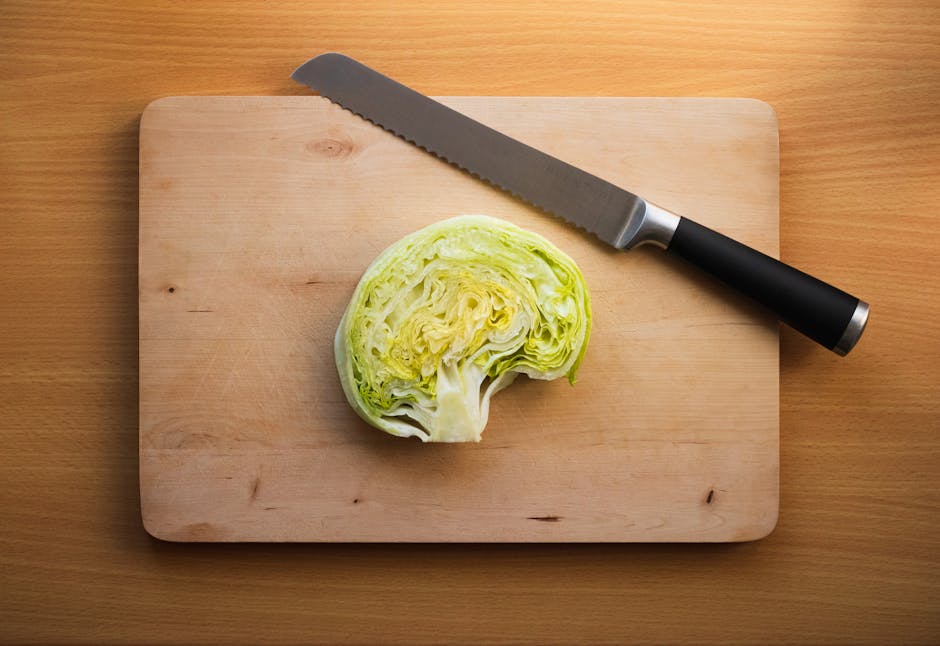 Half a crisp iceberg lettuce on a wooden board with a serrated knife.