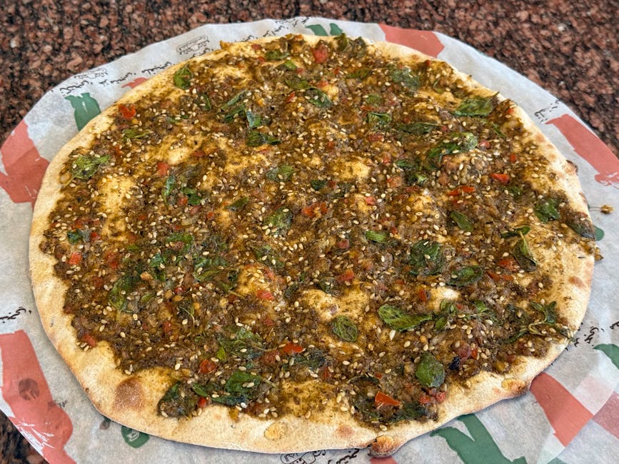 Freshly baked Middle Eastern manakish topped with zaatar and herbs on paper.