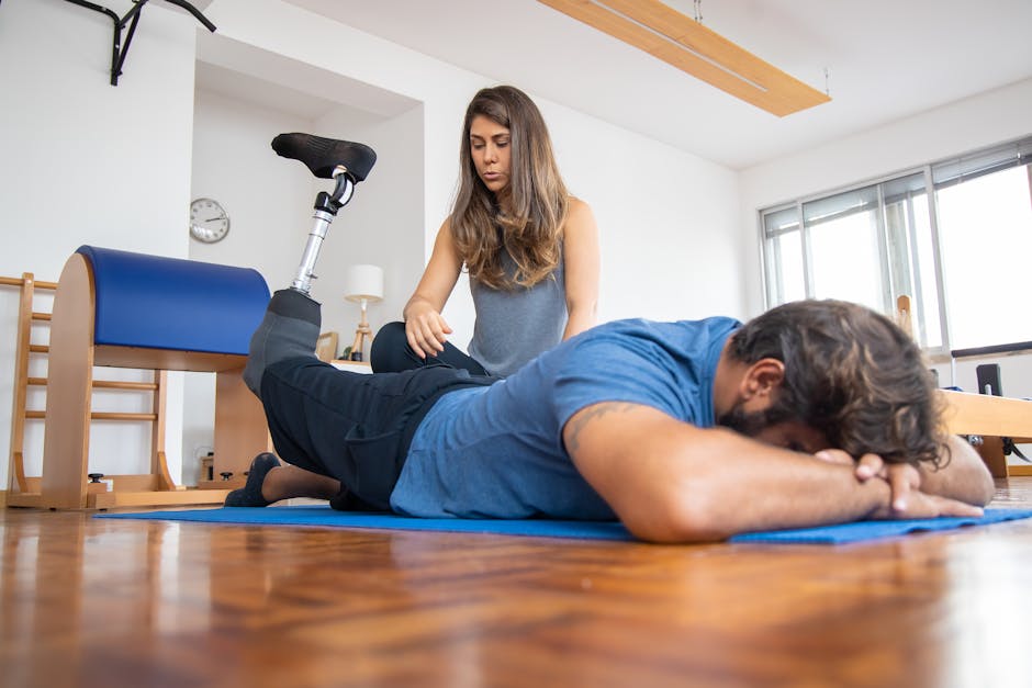 An adult man with a prosthetic leg receives physical therapy from a female trainer indoors.