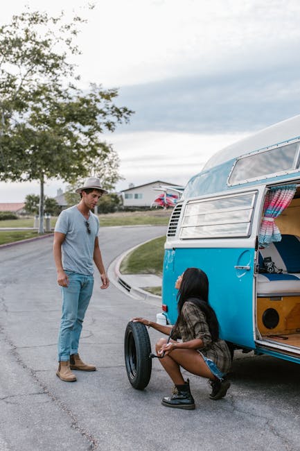 A young couple on a street fixing a flat tire on their vintage blue camper van.