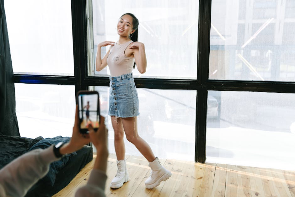 A young woman dancing while being recorded on a smartphone in a sunlit modern studio.