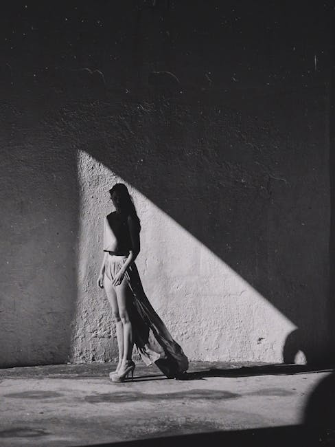 Stylish woman in long skirt and heels in dramatic light and shadow.