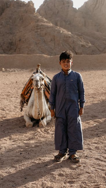 Boy in traditional clothing with camel in the arid desert of Sharm El-Sheikh, Egypt.