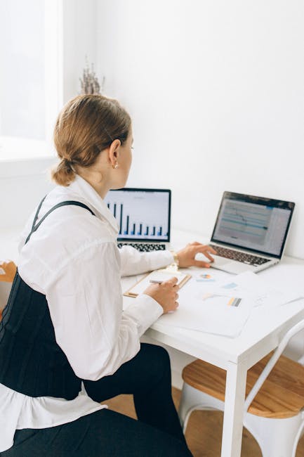 Woman using laptop for remote work in a bright home office setting, analyzing graphs.