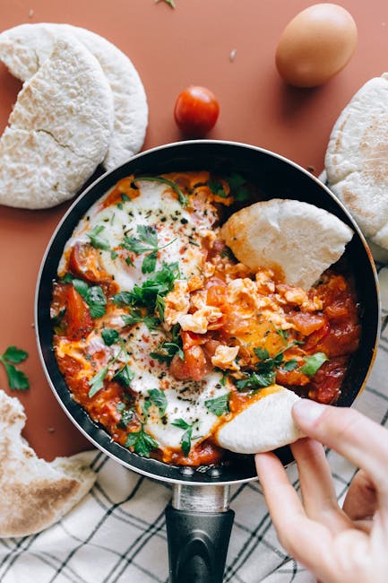 Savor a classic Shakshuka dish with vibrant tomatoes, eggs, and herbs served with fresh pita bread.