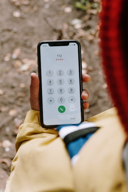 Close-up image of a hand dialing 112 emergency number on a smartphone outdoors.