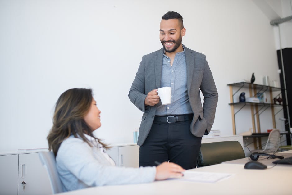 Two business professionals smiling and talking during a coffee break in a modern office setting.