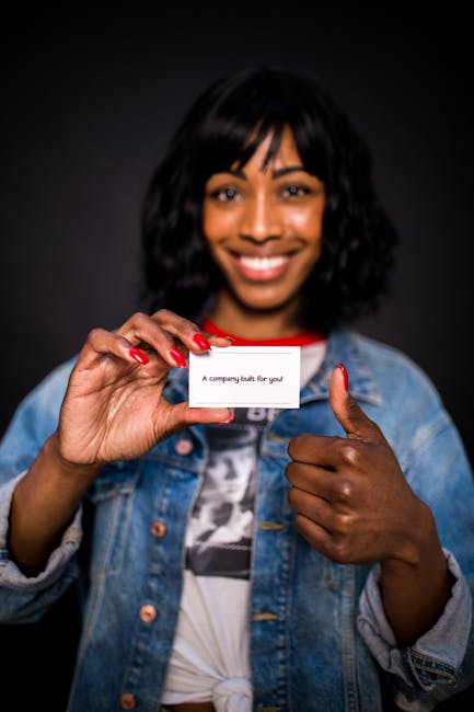 A cheerful woman in a denim jacket presents a business card with confidence.