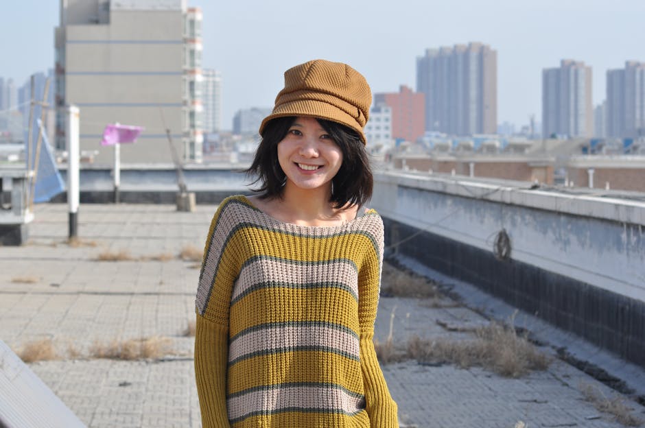 Smiling woman in a striped sweater and hat on a rooftop with city skyline.