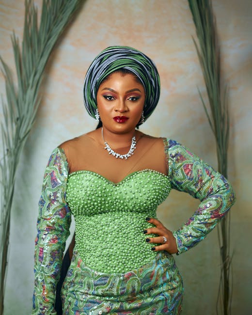 Confident woman in vibrant African attire with green gele and beaded gown.