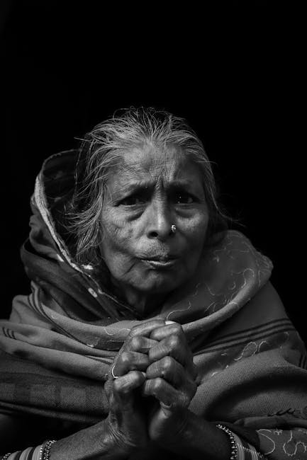 Black and white portrait of a senior woman with hands clasped, in traditional attire.