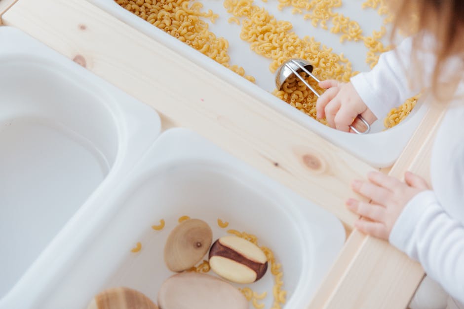 A child engaging in a fun sensory activity with uncooked pasta and wooden utensils indoors.