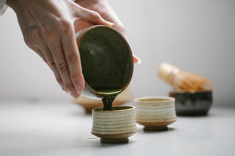 A traditional Japanese matcha tea ceremony with organic green tea being poured into ceramic cups.