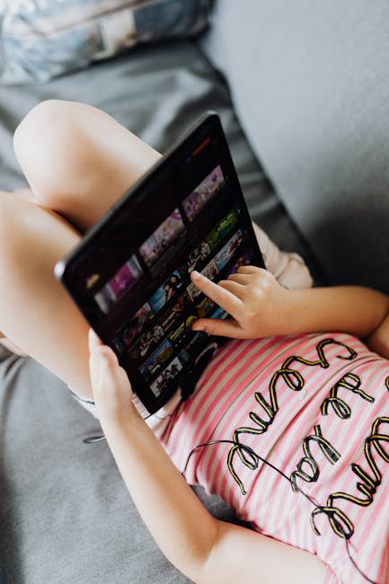 A young girl lying on a sofa using a tablet, browsing content with ease.