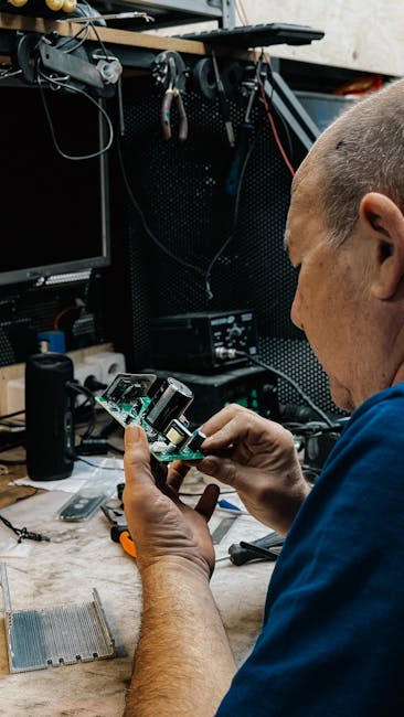 Technician fixing electronics amidst tools and gadgets at a cluttered workspace.