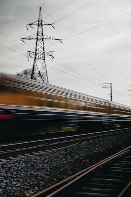 Blurred image of a high-speed train moving along steel tracks outdoors.