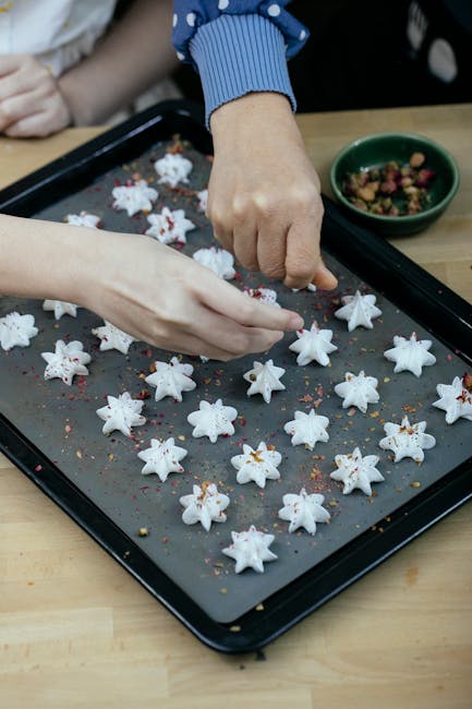 High angle of crop faceless ladies decorating freshly baked meringue cookies with flakes while preparing pastry for Christmas holidays