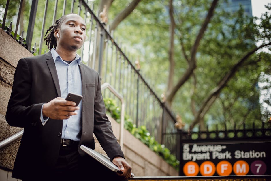 Confident businessman in a suit using a smartphone at Bryant Park Station entrance, NYC.